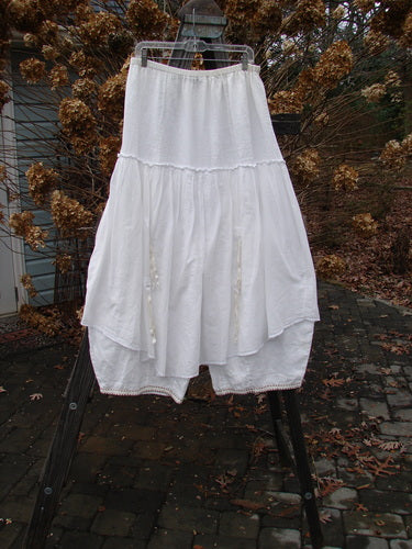 Barclay Hemstitch Embroidered Fusion Pant Skirt in unpainted white, size 2, on a clothes rack. Full elastic waistline, exterior lacy seams, tie accents, and cropped under pant with sectional panels. Tapered lowers and billowy shape for a special look. Pant measurements: waist 30-40, hips 62, inseam 20, full length 40. Upper layer measures 36 inches.