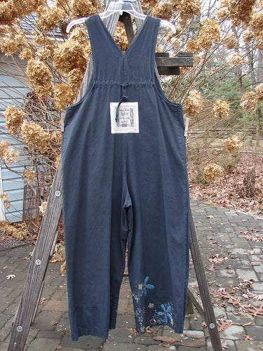 Image alt text: "2000 Parachute Overall Jumper Floral Black Size 0: Blue overalls on a wooden stand, featuring oversized front bib pocket, adjustable shoulder straps, deep side pockets, and wide swingy lowers."