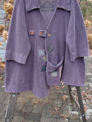 2000 PMU Celtic Moss Highlander Coat Aubergine Size 1: A purple coat on a rack, made from incredible Celtic Moss. Features include an empire waistline, multiple patches, and big collared front. Bust 56, waist 62, hips 72, hem circumference 90.