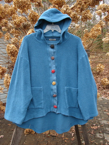 A blue jacket with buttons on a swinger, made from the incredible Celtic Moss. Features include a cozy hoodie, A-line shape, front drop pockets, and oversized fancy buttons. Perfect condition, size 2.