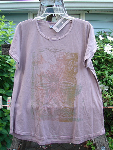 Barclay NWT Cap Sleeved Travel Tee features a rounded neckline, wide cap sleeves, and an A-line shape with a varying hemline, showcasing a subtle single flower theme in Rose Earth.