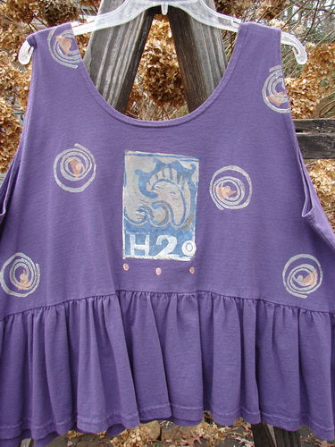 1992 Peplum Top Spinner Deep Violet OSFA: A rare vintage flounce top with a graphic design. Features a yoked waist seam, rounded neckline, and wide waist measurement. Signature Blue Fish patch and gathered bottom flounce. Bust 50, Waist 54, Hem Circumference 100, Length 25.