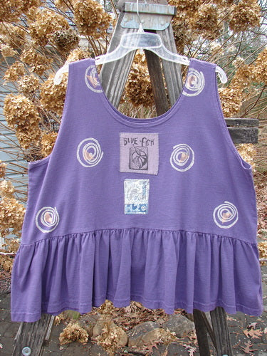 1992 Peplum Top Spinner Deep Violet OSFA: A patterned purple tank top with a yoked waist seam, rounded neckline, and wide waist. Features a gathered bottom flounce and a vintage H2O spinner theme.