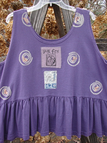 1992 Peplum Top Spinner Deep Violet OSFA: A purple tank top with a patch and design. Features a yoked waist seam, rounded neckline, wide waist, and gathered bottom flounce.