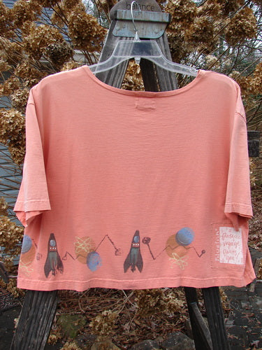 2000 Short Sleeved Crop Tee Rocket Coral Size 1: A pink shirt with a picture of a rocket in space, featuring a wider neckline and a super wide crop box shape.