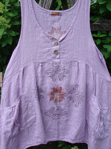 Barclay Linen Tuesday's Pocket Prairie Dress in Celtic Floral Lilac Size 1, featuring a sleeveless V-neck design with shell buttons, pleated empire waist, diagonal pockets, and mandala print, hanging on a wooden trellis.