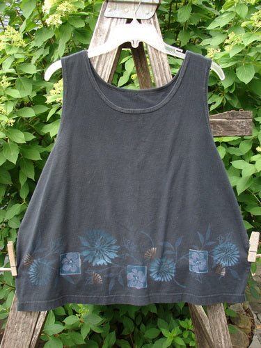 Barclay Cotton Lycra Tank Border Garden Black Size 2, featuring a loose-cut, sleeveless design with floral motifs along the hem, is displayed on a wooden ladder against a lush green backdrop.