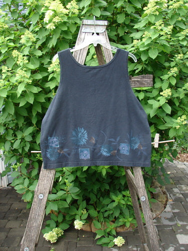 Barclay Cotton Lycra Tank Border Garden Black Size 2 draped on a rustic ladder, featuring a faded floral pattern along the hem, set against a garden backdrop with lush foliage and hydrangeas.