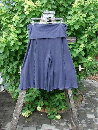 Barclay Thermal Fold Over Crop Pant Unpainted Deep Violet Size 1 displayed on a clear hanger against a lush green hedge, highlighting its slouchy, knee-length design and knit texture, embodying vintage Blue Fish Clothing style.