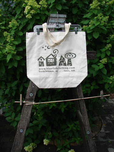 Barclay Canvas Promo Tote Bag Store Locations Natural One Size hanging on a wooden ladder, featuring whimsical house icons, a crescent moon, stars, and store locations Frenchtown, NJ and Taos, NM printed below.