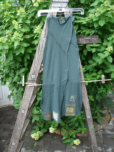 Barclay Thermal Patched Curvy Scarf Army Forest OSFA drapes on a wooden ladder, showcasing its asymmetrical seam and decorative patches. Its waffle texture and curly edges highlight the creative BlueFishFinder style.