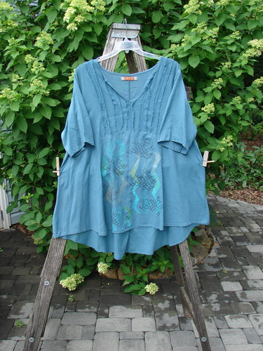 Barclay Batiste Flutter Bib Tie Back Dress Honeycomb Tealen Size 1: A teal-blue tunic with a V-neck, pintuck detailing, and wavy-line print, displayed on a stepladder, embodying vintage Blue Fish Clothing style.