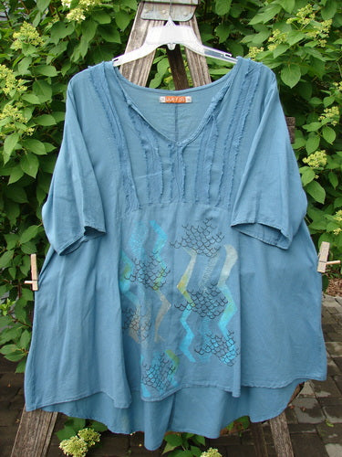 Barclay Batiste Flutter Bib Tie Back Dress Honeycomb Tealen Size 1, featuring a loose fit, pintuck stitching, and pastel geometric print, draped over a wooden stepladder amidst lush foliage.