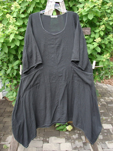 Barclay Gauze Urchin Bell Dress Unpainted Black Size 1 displayed on a wooden drying rack, features a scoop neckline, elbow-length sleeves, asymmetrical hem, and draped side pockets, embodying Bluefishfinder.com's creative vintage style.