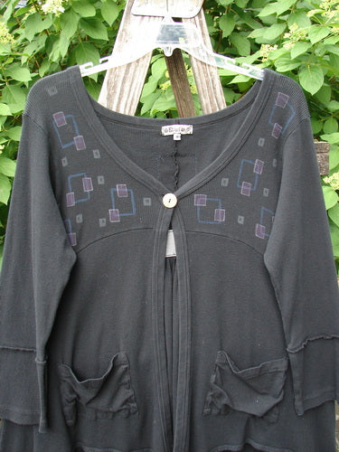 Barclay Patched Thermal Single Button Cardigan Tiny Square Black Size 0, features a single wooden button, exterior pockets, and geometric squares in muted purples and greys, hanging outdoors against greenery.