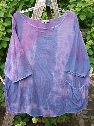 Barclay Gauze Round Bottom Tie Back Pocket Top Mottled Purple Dusk Size 2, featuring a loose, crinkled texture with a scooped neckline and three-quarter sleeves, elegantly drapes against a lush green backdrop.