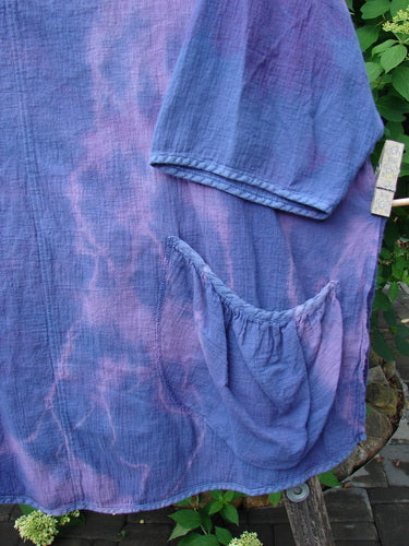 Barclay Gauze Round Bottom Tie Back Pocket Top Mottled Purple Dusk Size 2, featuring a loose-weave design with three-quarter sleeves and a gathered pocket, displayed outdoors against green foliage.