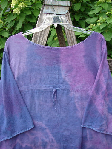 Barclay Gauze Round Bottom Tie Back Pocket Top in Mottled Purple Dusk, Size 2, displayed on a clear hanger against a wooden ladder, showcases its loose fit and long sleeves in soft, gauzy fabric.