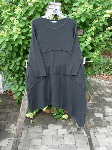 Barclay Thermal Exterior Stitch Three Tier Dress Unpainted Black Size 2 displayed, featuring a loose fit, asymmetrical hem, and subtle horizontal seams, made from soft knit fabric, hanging on a wooden ladder.