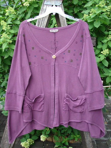 Barclay Patched Thermal Single Button Cardigan Tiny Square Murple Size 1, featuring an asymmetrical hem, square embellishments, wooden button closure, and gathered pockets, displayed on a wooden ladder amidst greenery.