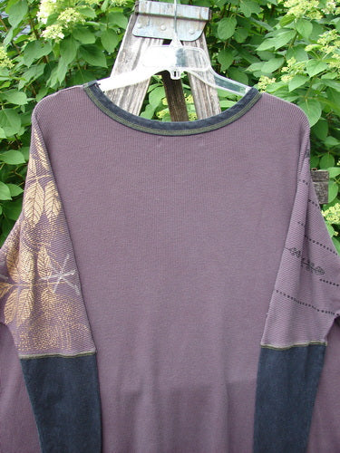 Barclay Thermal Contrast Revival Top Metallic Leaf Brum OSFA hangs on a wooden ladder, showcasing its distinct contrasting sleeves and botanical print. The rounded neckline and side vents enhance its unique design.