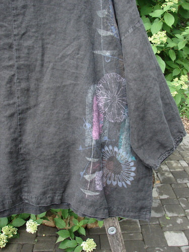 Barclay Linen Lantern Boxy Top Side Floral Black Size 1 with wide three-quarter sleeves, pastel floral motif near hem, displayed on a wooden stool outdoors against a backdrop of green shrubs.