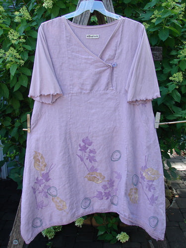 Barclay Linen Lace Blooming Tunic Dress Leaf Vine Lavender Size 0: A loose-fitting, short-sleeved tunic with a crossover button neckline, featuring floral and leaf motifs on the hem, hanging against greenery.
