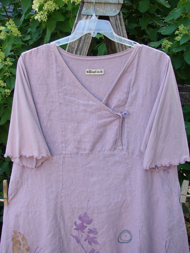 Barclay Linen Lace Blooming Tunic Dress Leaf Vine Lavender Size 0, featuring a V-neck wrap-style bodice, elbow-length sleeves, and a lace-trimmed hem with botanical prints, displayed outdoors on a wooden ladder.
