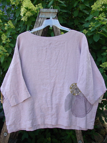 Barclay Linen Lantern Boxy Giant Blossom Hydrangea Size 1 displayed on a hanger over a ladder, showcasing its loose fit, three-quarter sleeves, round neckline, and a hand-stitched appliqué.