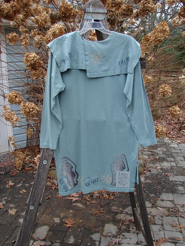 1996 Trifocal Top Celestial Trinket Size 1: A long-sleeved blue shirt with a rear shirttail hemline and folded collar, featuring a painted abstract forest theme and Blue Fish patch.