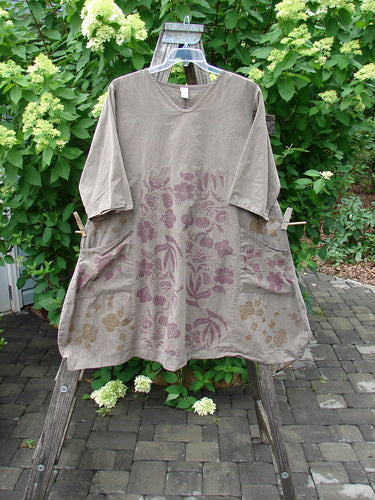 The Barclay Percal Urchin Dress, in Climbing Garden Stripe Rock Size 0, features a taupe top and floral-patterned skirt with front pockets, draped over a wooden stepladder outdoors.