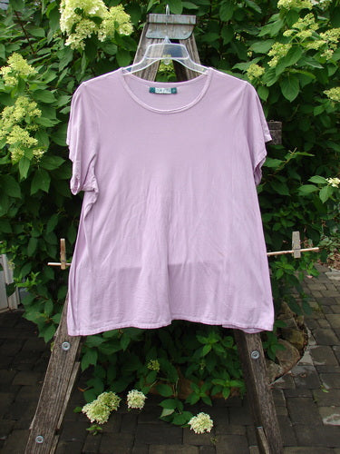 Barclay Cap Sleeved Tee Unpainted Lavender Size 2 hanging outdoors on a clear plastic hanger against a backdrop of green foliage and hydrangeas, embodying Bluefishfinder.com's vintage and creative expression ethos.