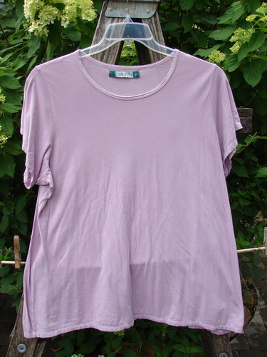 Barclay Cap Sleeved Tee Unpainted Lavender Size 2, featuring a crew neckline and short sleeves, hangs on a clear hanger against lush greenery, embodying Bluefishfinder.com's vintage, expressive style.