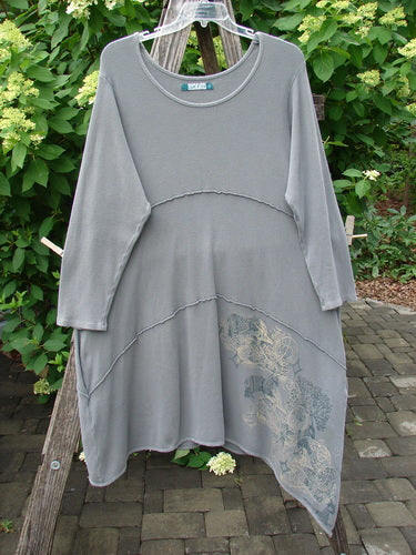 Barclay Thermal Exterior Stitch Three Tier Dress Forest Friend Grey Day Size 2: A long-sleeve tunic dress featuring an asymmetrical hem, exposed overlock seams, and a subtle botanical print on the lower right side.