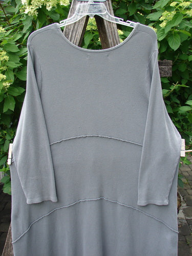 Barclay Thermal Exterior Stitch Three Tier Dress, Forest Friend Grey Day Size 2, hangs on a clear hanger, featuring two horizontal seams and many tiny pulls, set against leafy greenery.
