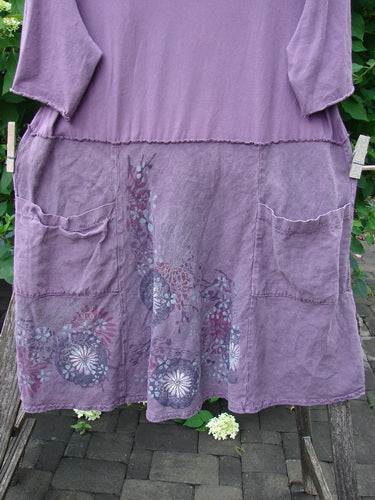 Barclay Linen Cotton Two Pocket Tie Back Square Dress Bloom Burst Plum Size 1 featuring a loose fit, patch pockets, scalloped waist, and decorative floral hem, hanging on a clothesline outdoors.