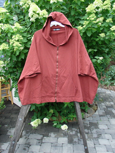 Barclay PMU Patched Hooded Postcard Zipper Jacket Vest in Deep Brick features a relaxed fit, dolman shoulders, batwing sleeves, and two front patch pockets, hanging on a wooden ladder outdoors.