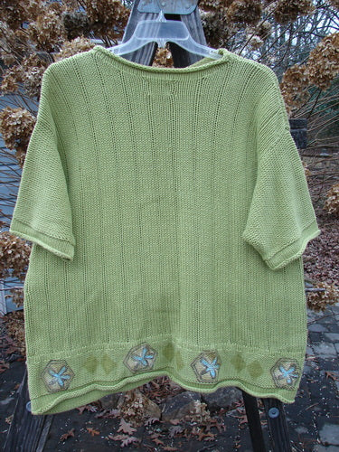 1999 Spring Pullover Tunic Sweater Kiwi Size 2: A green sweater with a flower design on a clothes rack.