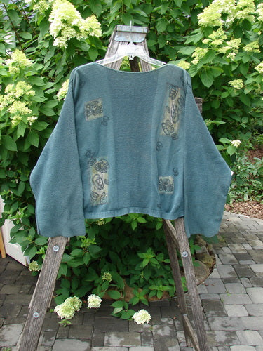 1994 Panel Cardigan Sweater Magic Tea Party Nightshade OSFA, featuring a boxy shape, contrasting fabric patches, drop shoulders, and fold-over belled sleeves, displayed over a wooden ladder.