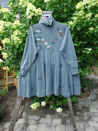 1996 Enchantment Dress Polka Path Mirror Size 2, a loose-fitting slate-blue dress with abstract prints, ribbed turtleneck, empire waist, sweeping skirt, and exterior stitching, draped on a wooden stepladder outdoors.