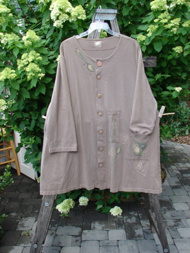 1999 Silverware Top Reverse Dining Riverbed OSFA, an oversize taupe tunic with wood-tone buttons, spiral and leaf motifs, and unique pencil pockets, draped on a wooden ladder outdoors.