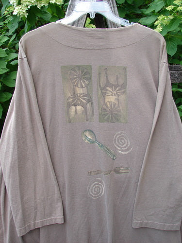 1999 Silverware Top Reverse Dining Riverbed OSFA featuring a taupe long-sleeved T-shirt with unique back graphic design elements of rectangles, utensils, and spirals, hanging against a leafy backdrop.