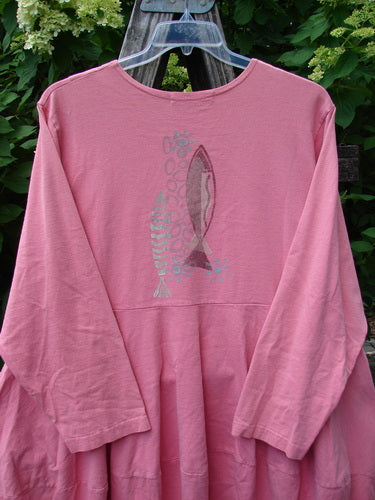 1997 Brenton Dress Two Fish Tulip Size 2, a loose-fitting, long-sleeved pink dress with a unique sectional skirt and two stylized fish graphic, hanging from a clear hanger outdoors.