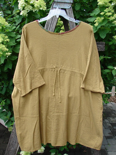 Barclay Gauze Round Bottom Tie Back Pocket Top Ditsy Daisy Golden Size 2, shown on a hanger with elbow-length sleeves and waist drawstring, set against lush greenery.