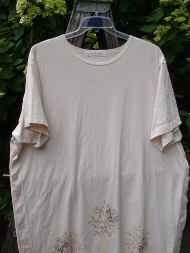1997 Mauritius Top Sea Coral Powder OSFA: A pale-cream, oversized tunic with short sleeves, featuring a subtle floral motif near the hem. It hangs outdoors, highlighting its unique, wider square cut and side vents.