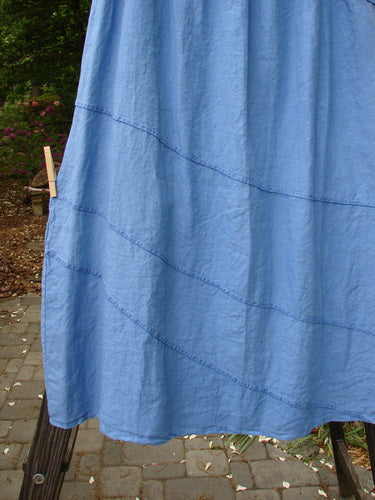 Image: A blue dress on a clothesline against a blue curtain with a clothespin. 

Alt text: Barclay Linen Diagonal Skirt, a blue dress hanging on a clothesline against a blue curtain.