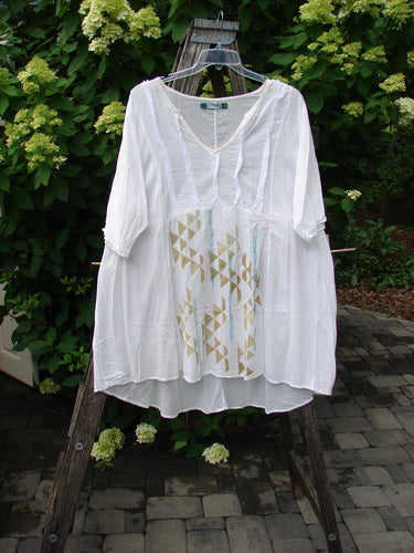 Barclay Batiste Flutter Bib Tie Back Dress Triangular Geo White Size 2, featuring a V-neck and elbow-length sleeves with a subtle geometric print, draped on a wooden ladder.