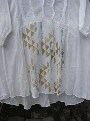 Barclay Batiste Flutter Bib Tie Back Dress in Triangular Geo White, Size 2, features a gathered yoke, billowy body, tiered hem, with gold triangles and turquoise lines printed on the front.