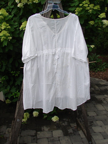 Barclay Batiste Flutter Bib Tie Back Dress in Triangular Geo White, Size 2, hangs outdoors, showcasing its loose, knee-length cotton design against a leafy backdrop, embodying Bluefishfinder.com's vintage, expressive style.