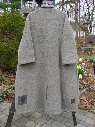 Vintage grey wool coat on rack, close-up of tree and stone walkway.